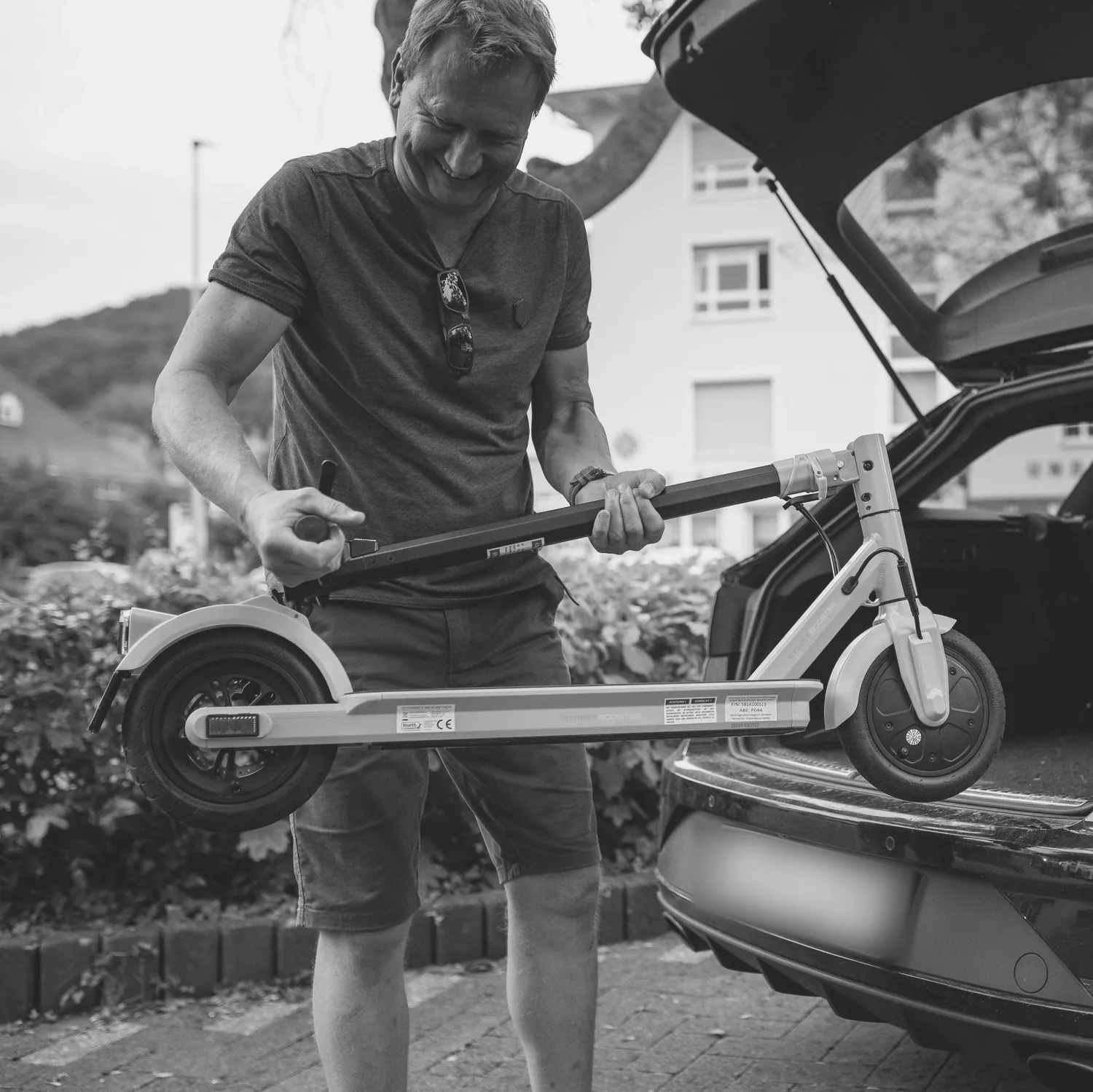 Mann hebt einen zusammengeklappten E-Scooter in den Kofferraum