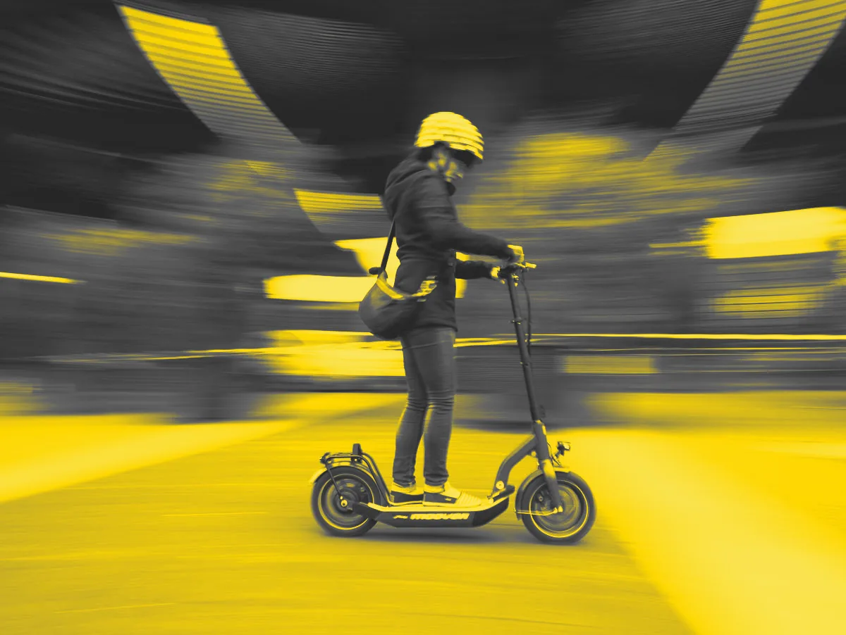 Frau mit Helm fährt auf einem E-Scooter, die Umgebung verschwimmt im Tempo