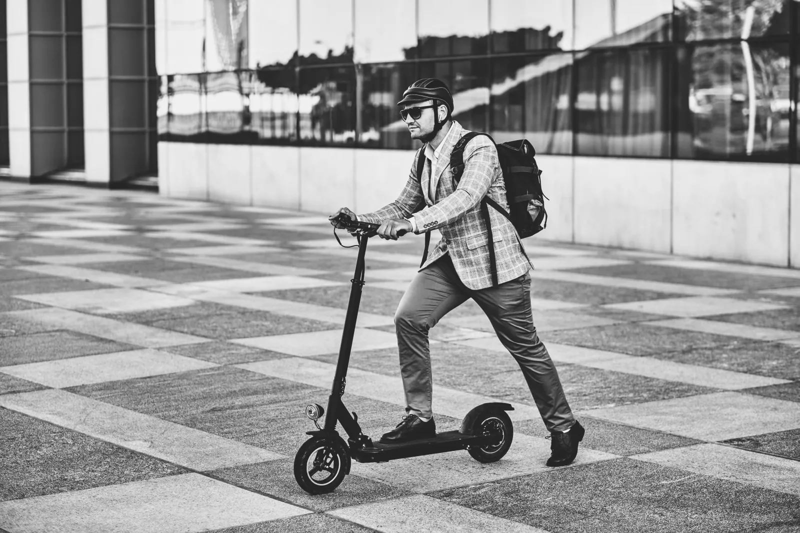Mann mit Rucksack fährt auf einem E-Scooter über einen Platz
